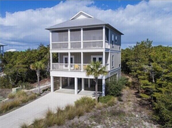 Une maison à deux étages située en bord de mer, dotée d’un balcon à l’étage supérieur et entourée de végétation.