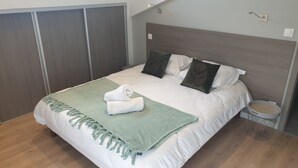 Siististi pedattu sänky, jossa on vihreä heittopeitto, valkoiset tyynyt ja harmaa pääty.
