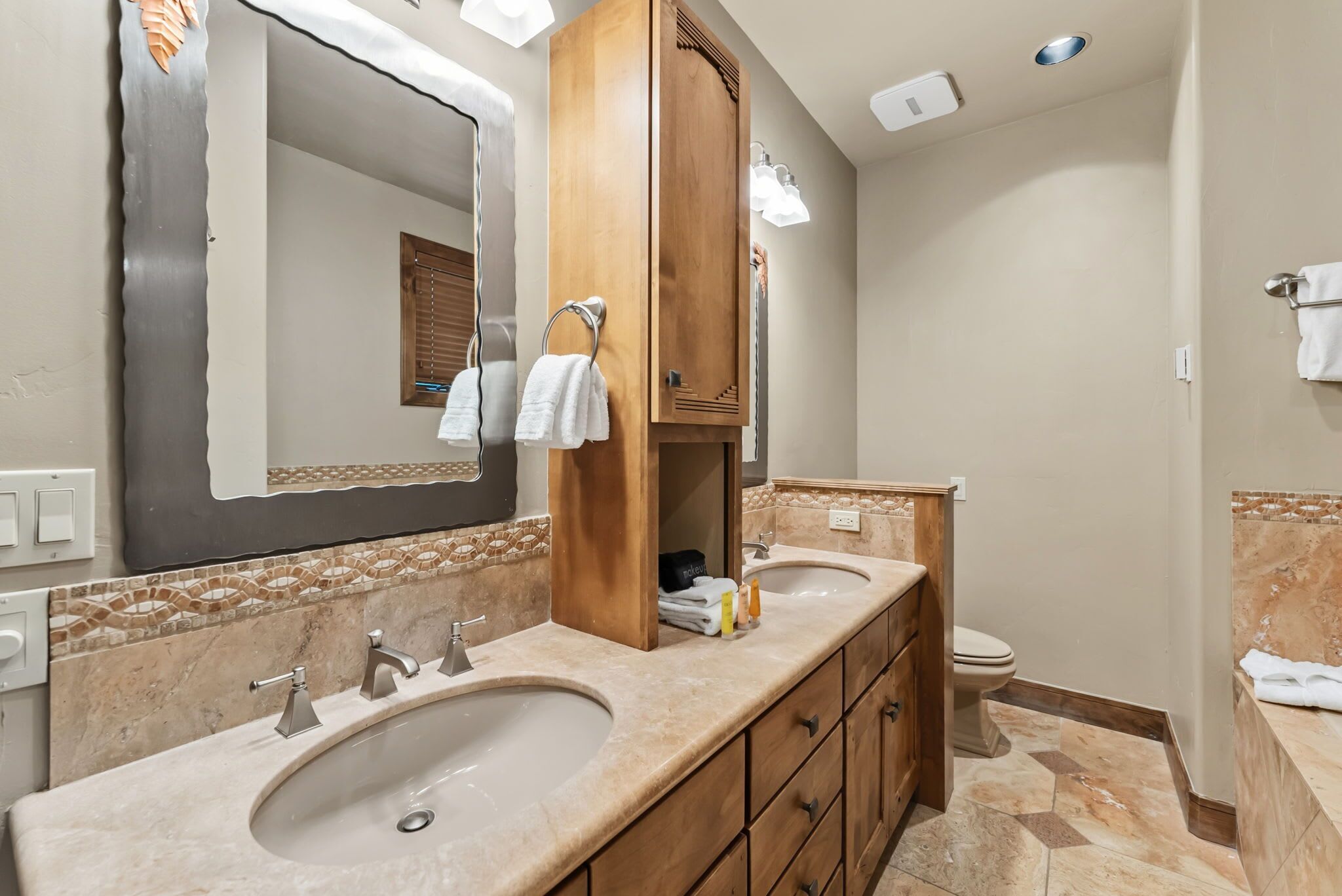 A bathroom with two sinks, a mirror, a wooden cabinet, and a toilet.