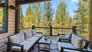 A wooden deck with a sofa and table, surrounded by a railing, overlooking a forest.