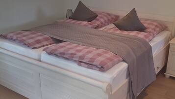 Una cama doble con cabecera blanca, dos almohadas y una manta rosa a cuadros.