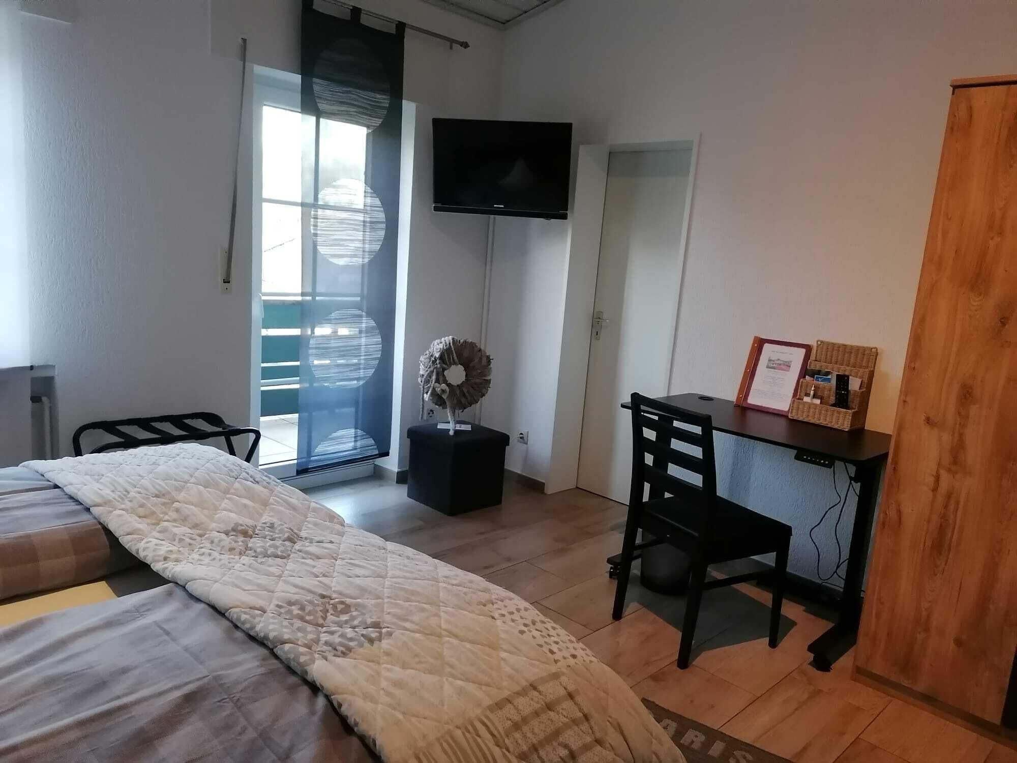 Un dormitorio con cama, escritorio, silla, televisor y una puerta que da a un balcón.