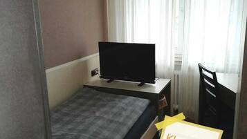 A small, single-bed room with a television on a stand, a desk, and a chair.