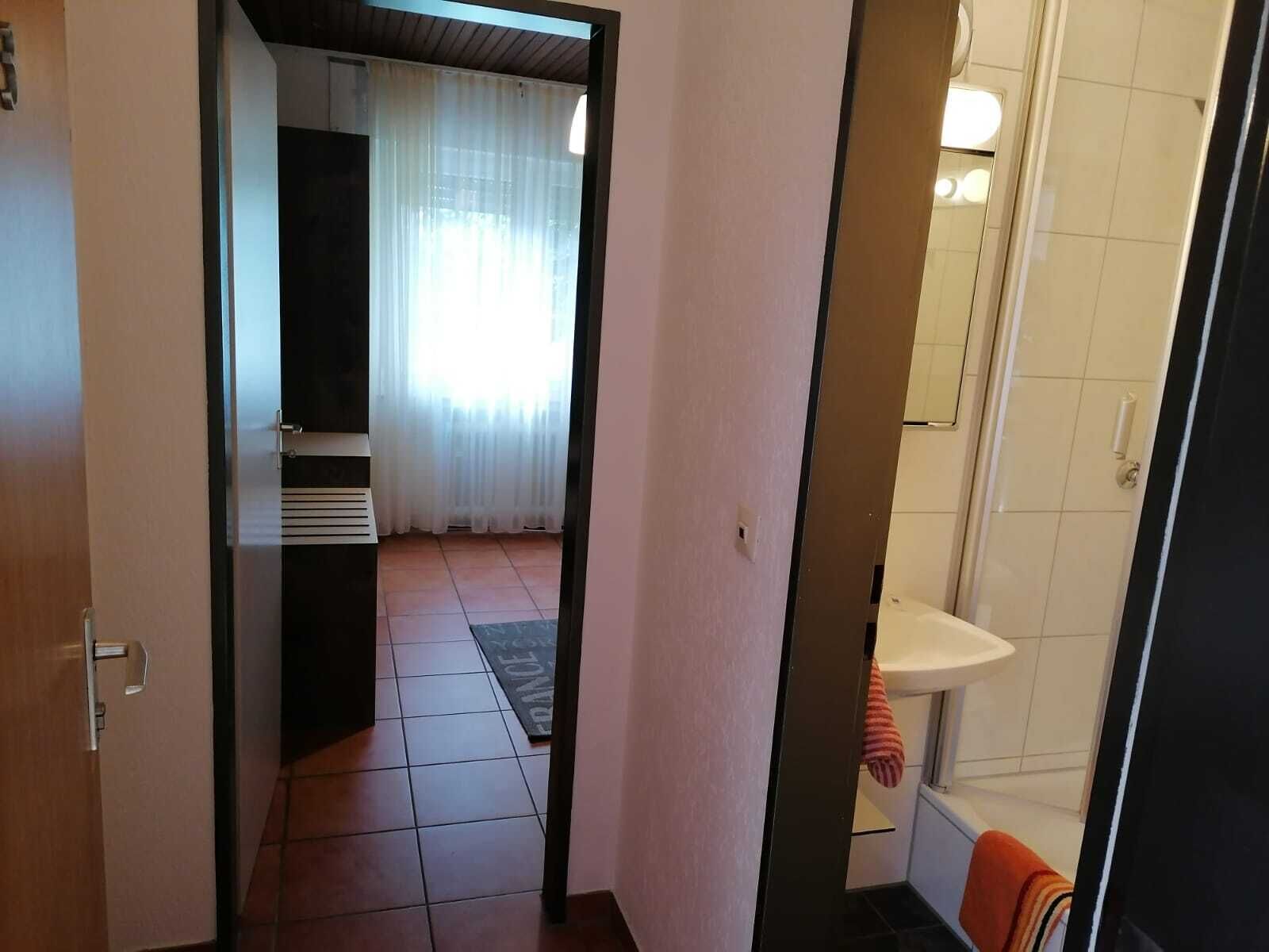 A narrow hallway leading to a bathroom with a shower, a towel hanging on the wall, and a door on the left.