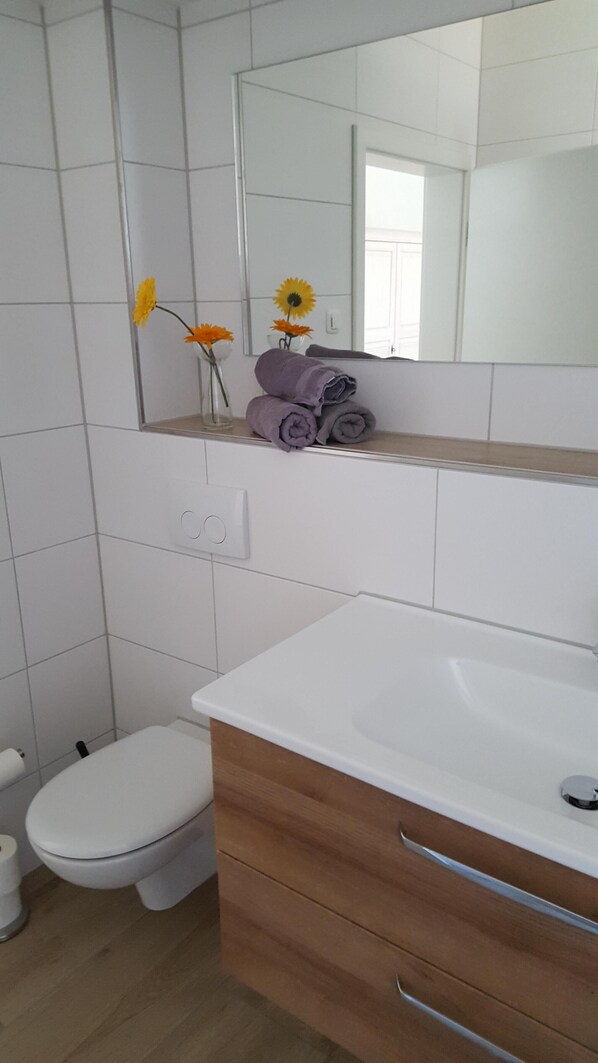Un baño con lavamanos blanco, tocador de madera, inodoro y espejo sobre el lavamanos.
