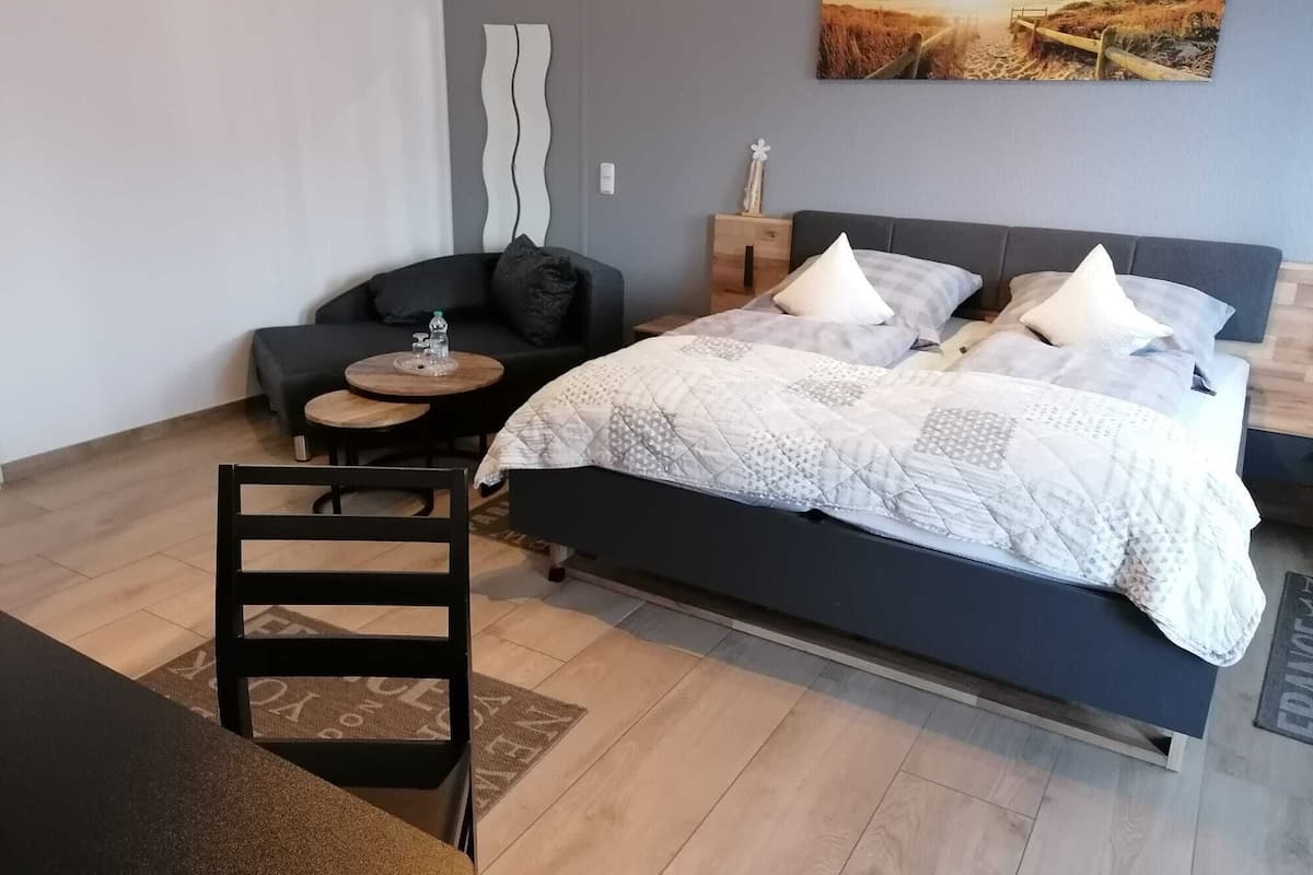A modern bedroom with a large bed, a sofa, a small round table, and a chair.