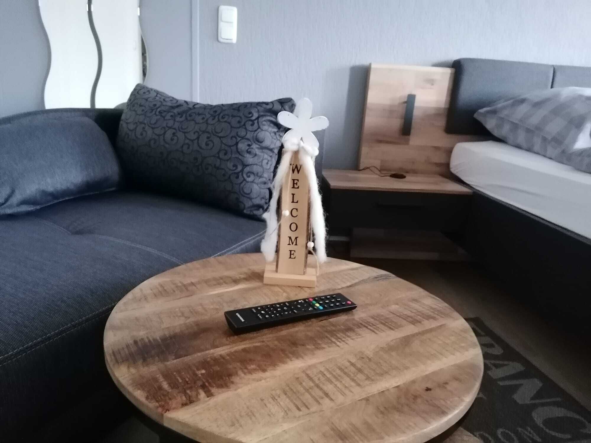 A modern living room with a round wooden coffee table, a remote control, and a 'WELCOME' sign.