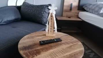 A modern living room with a round wooden coffee table, a remote control, and a 'WELCOME' sign.
