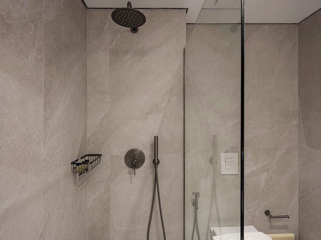 Ein modernes Duschbad mit Glastrennwand, Handbrause, am Wand montiertem Wasserhahn und einer kleinen Ablagefläche.