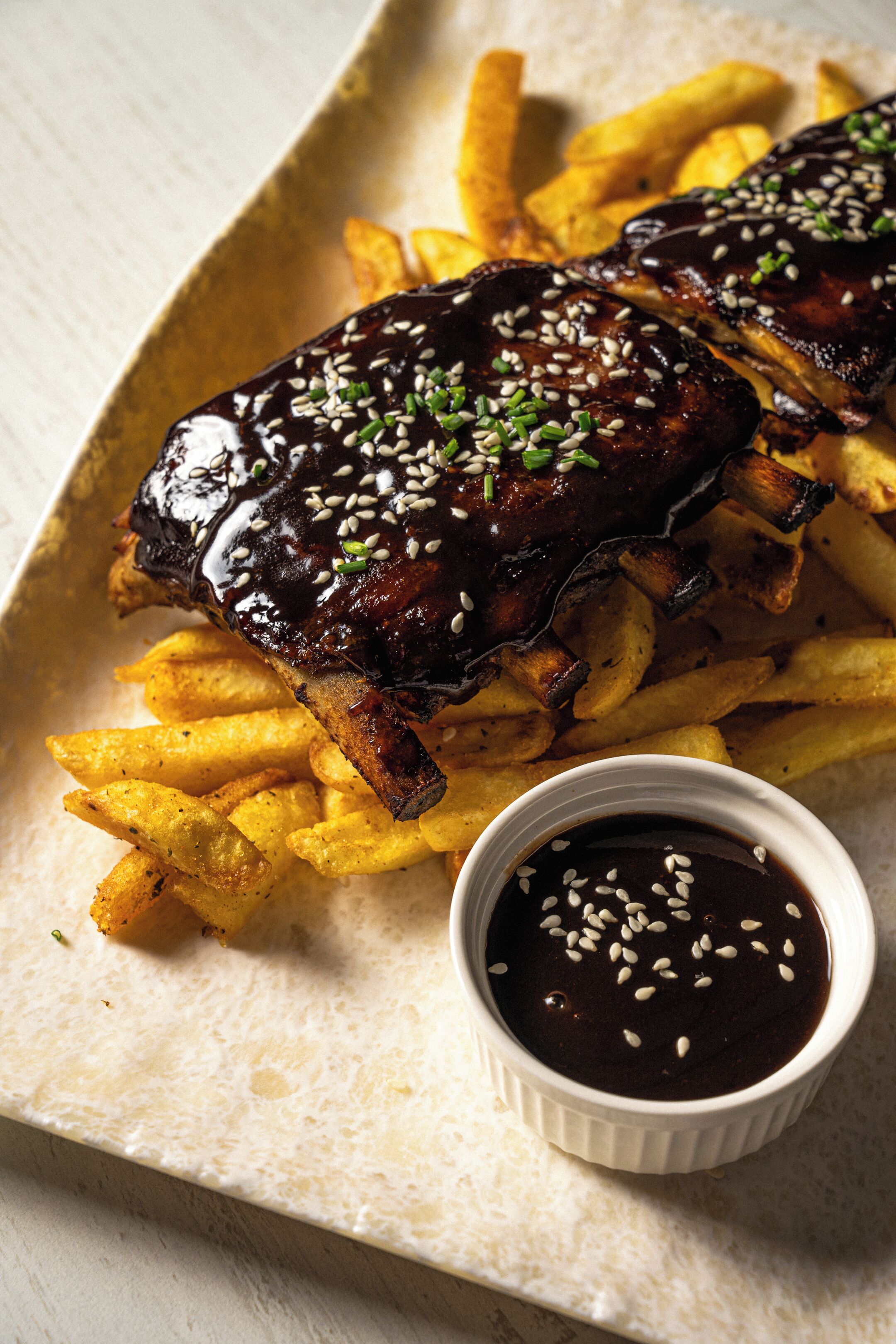 Un plato de costillas con papas fritas y salsa aparte.