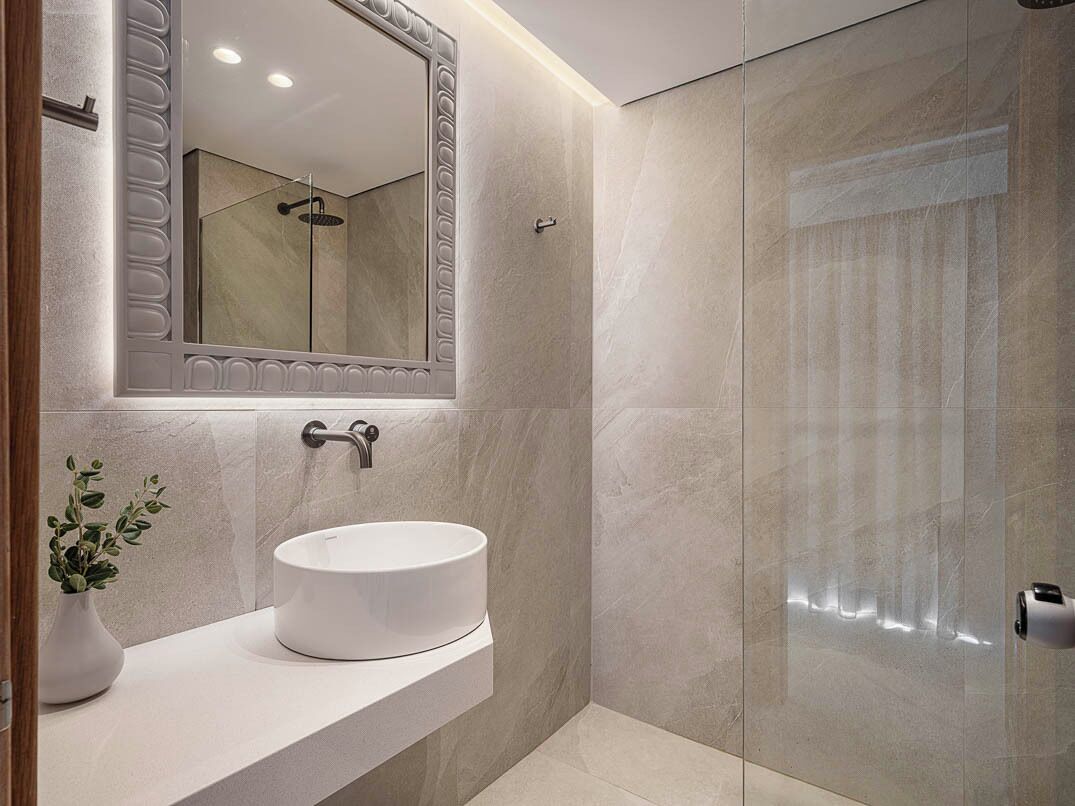 Un baño moderno con un lavamanos redondo, un espejo grande y una ducha con cerramiento de vidrio.