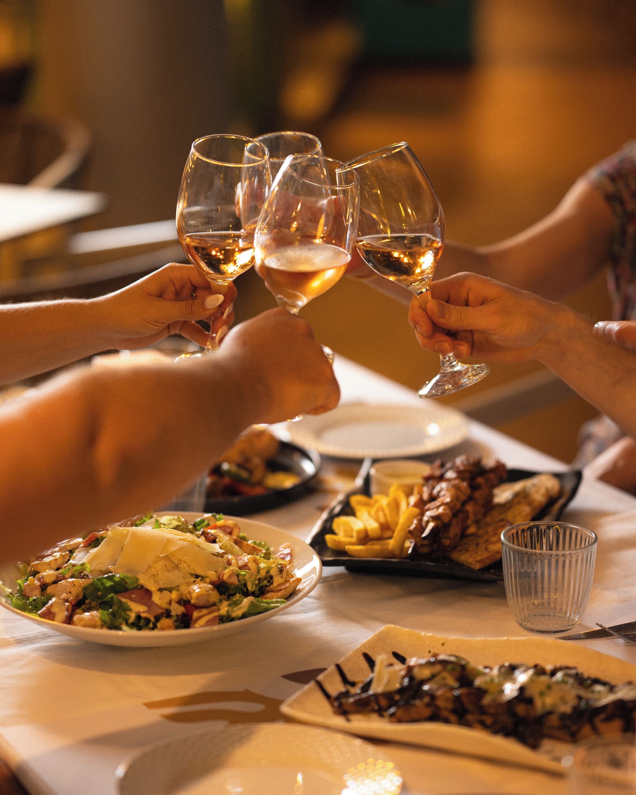 A dining table with plates of food, glasses of wine, and a clear glass.
