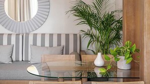 Ett modernt vardagsrum med ett matbord med glasskiva, en randig soffa, trästolar, en stor spegel och en hängande taklampa.