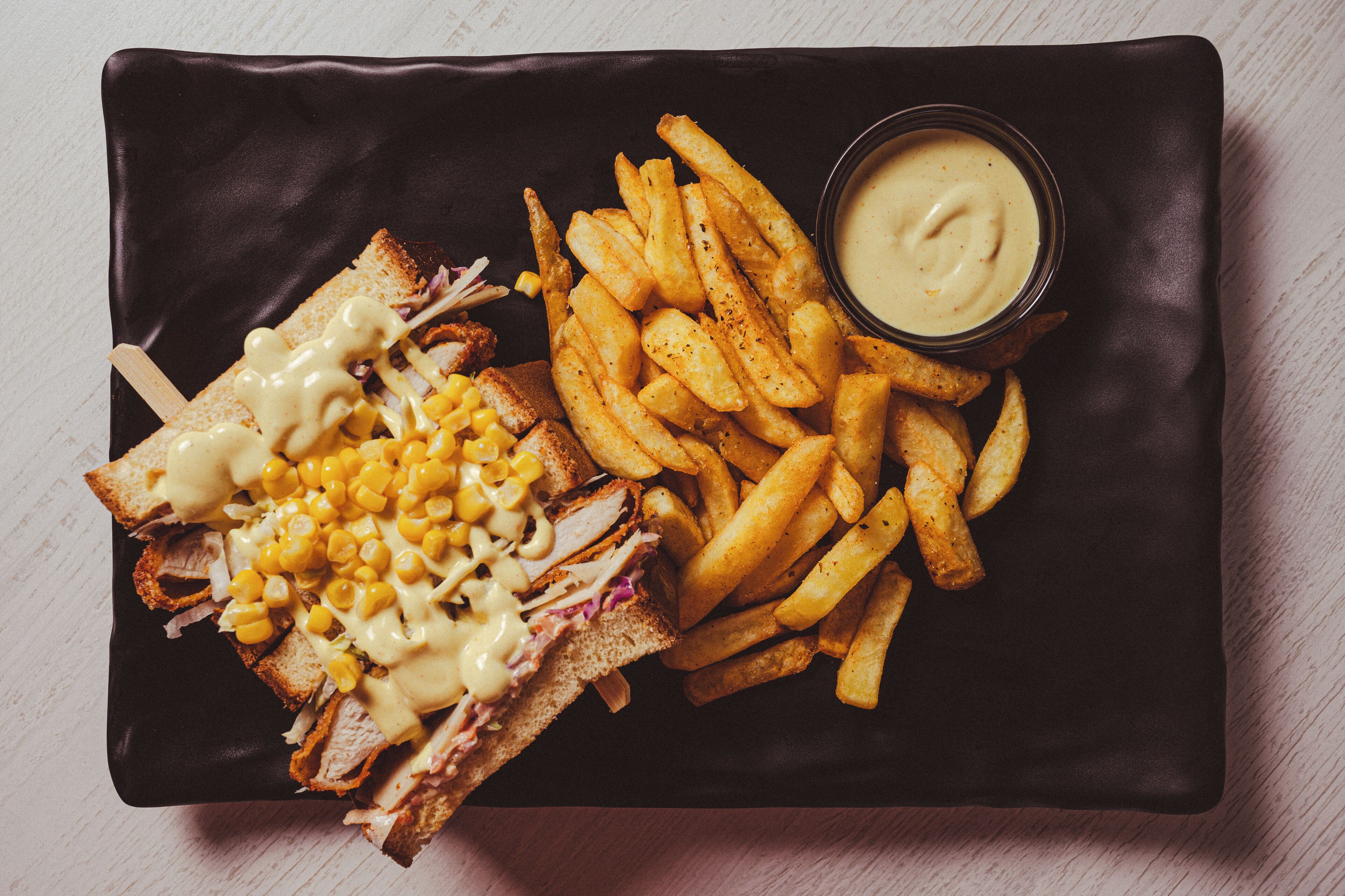 A sandwich with mac and cheese and a side of fries on a black plate.