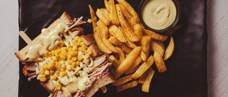 A sandwich with mac and cheese and a side of fries on a black plate.