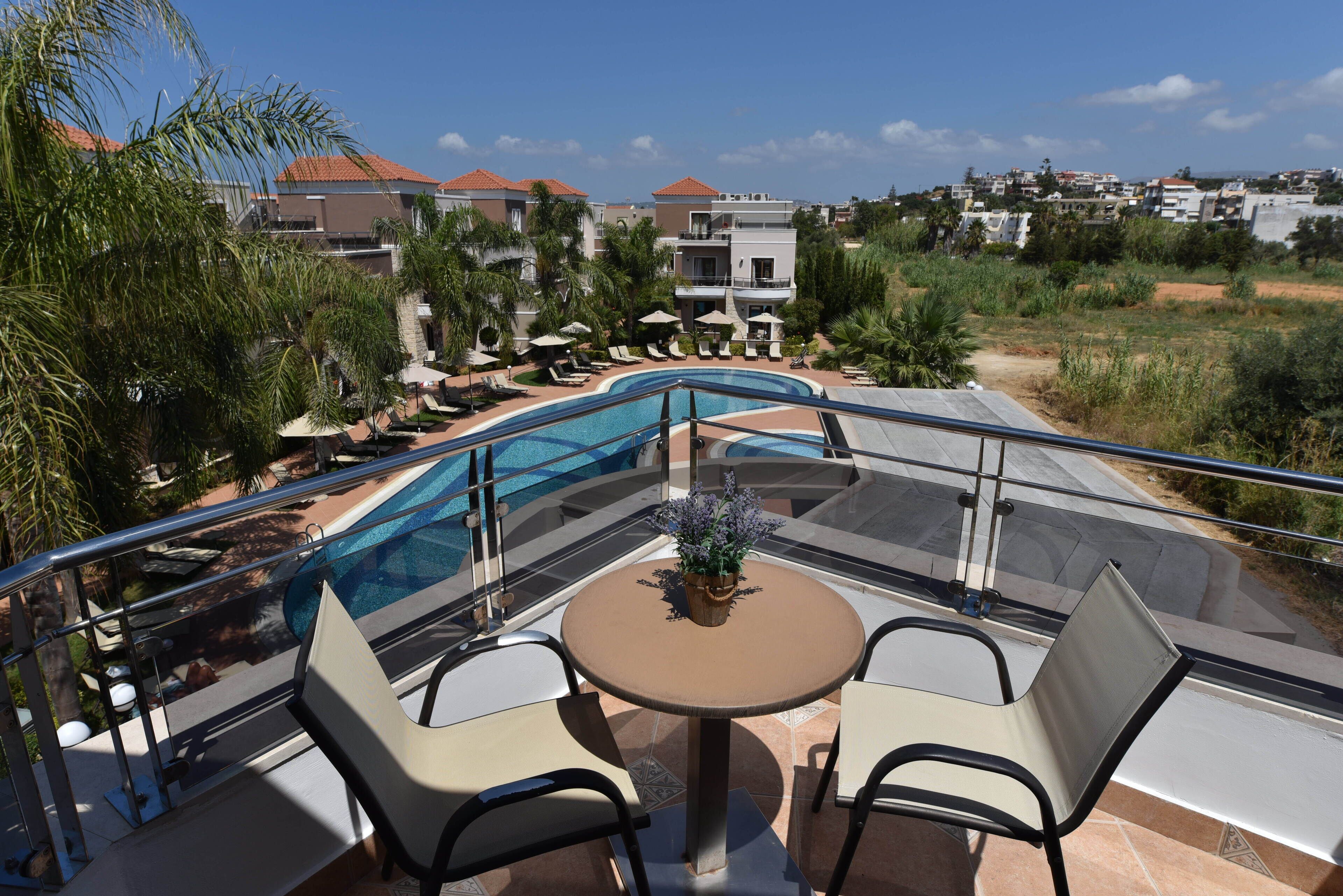 Un espace aménagé au bord de la piscine, doté d’une balustrade en verre, d’une table ronde avec des chaises, et offrant une vue sur les bâtiments et le paysage environnants.