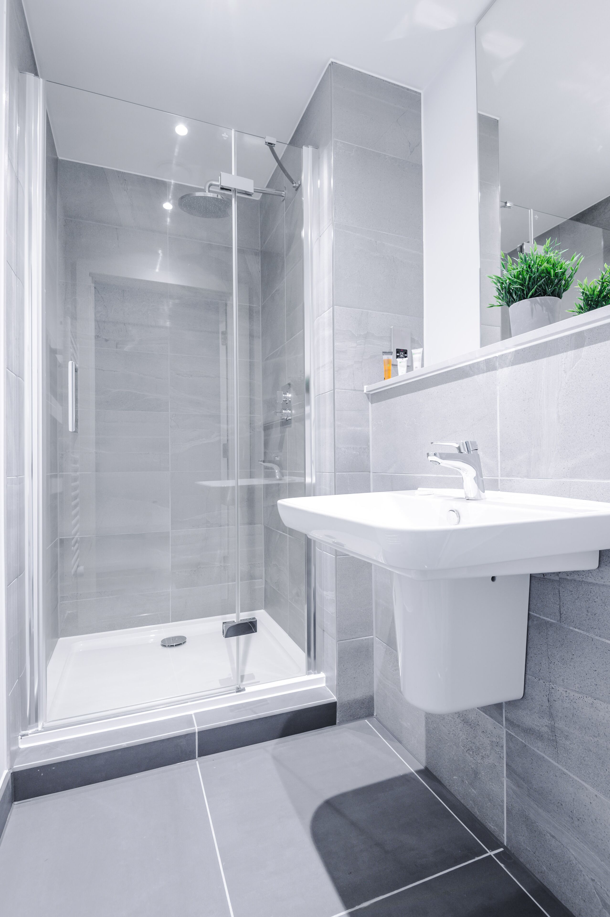 A modern bathroom with a glass-enclosed shower, a white sink, and grey tiled walls.