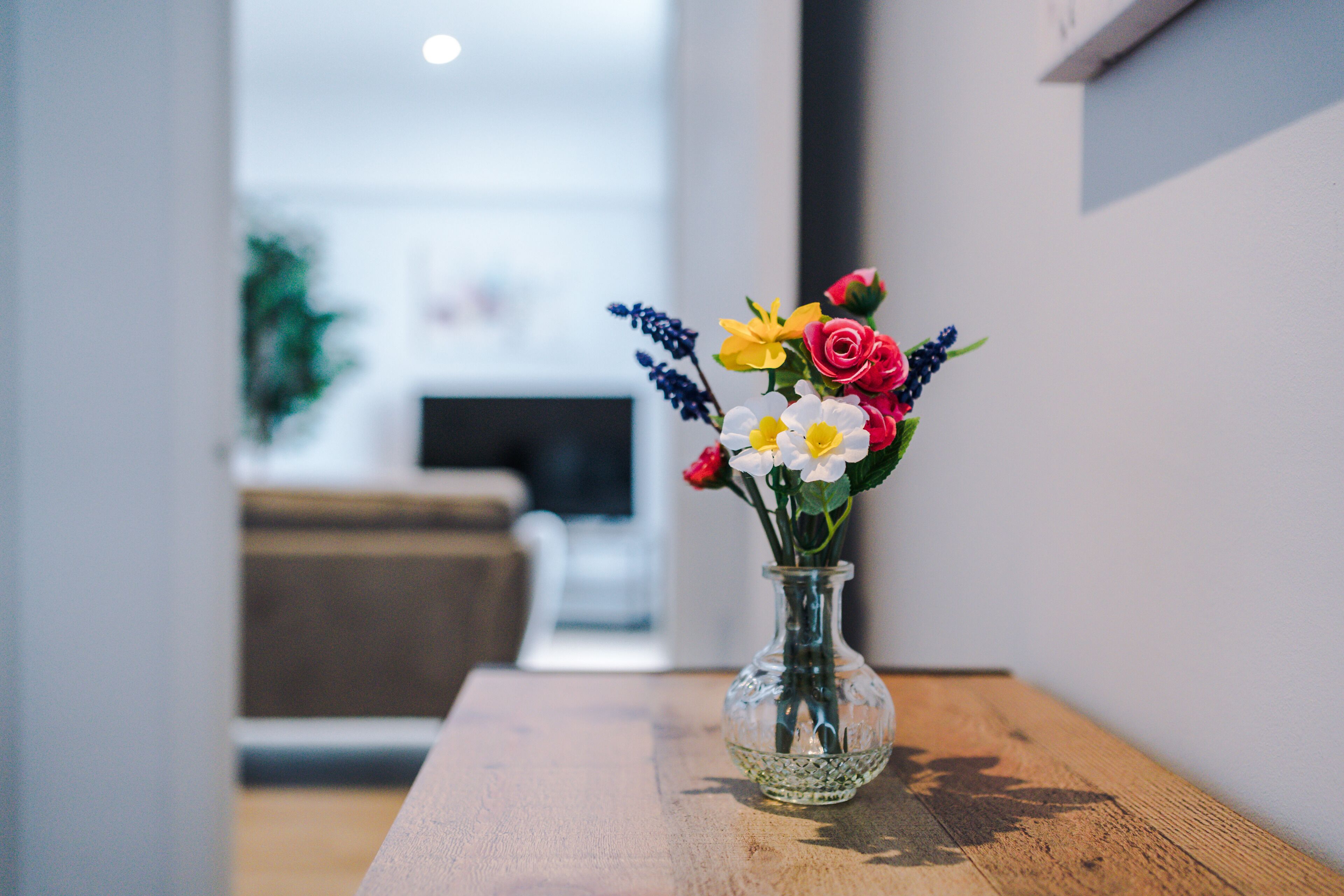 A clear view of a room with a wooden table, a glass vase with flowers, and a blurred background suggesting a living area.