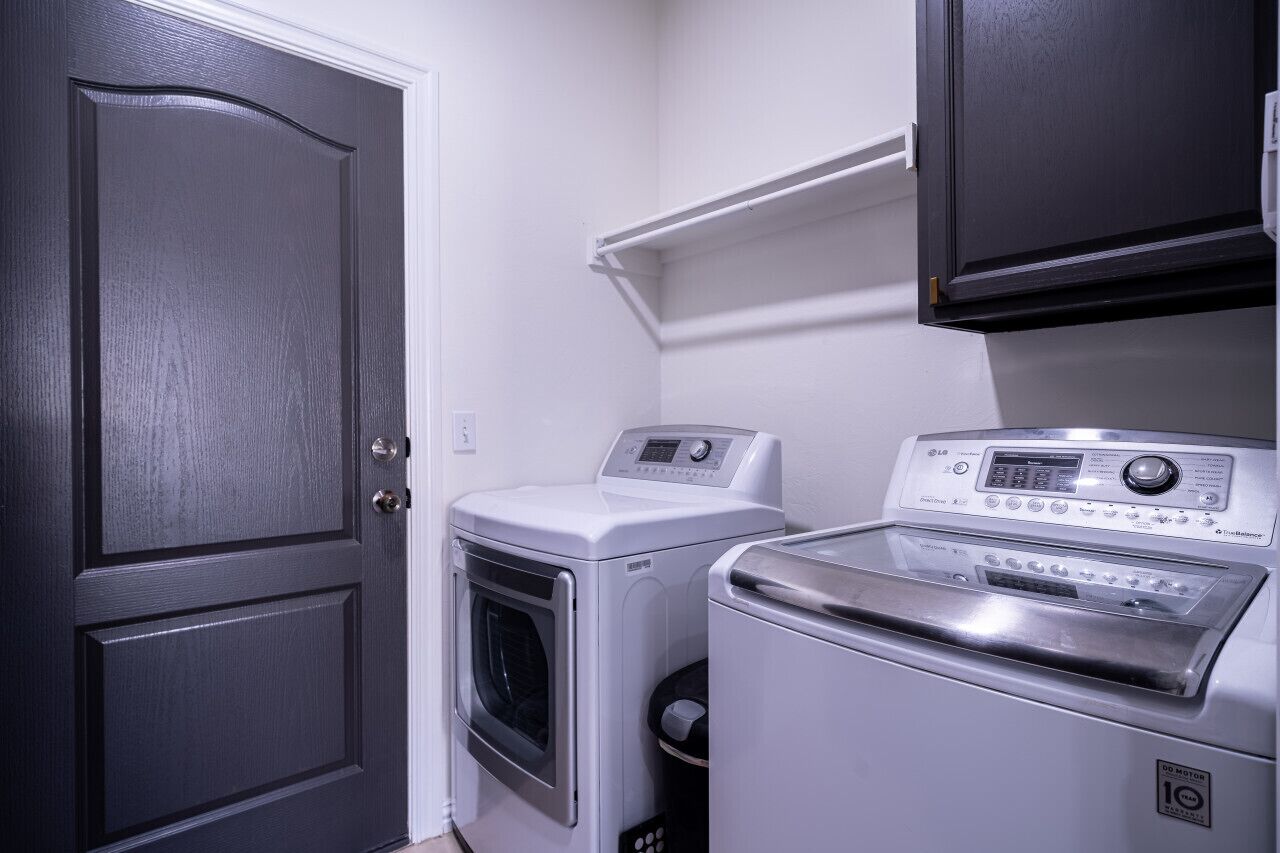 Une buanderie équipée d’un lave-linge et d’un sèche-linge à chargement frontal, d’une porte en bois foncé et d’un mur blanc.