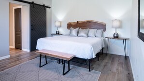 Ett sovrum med en säng, en bänk, två sängbord, en lampa och en stor spegel.