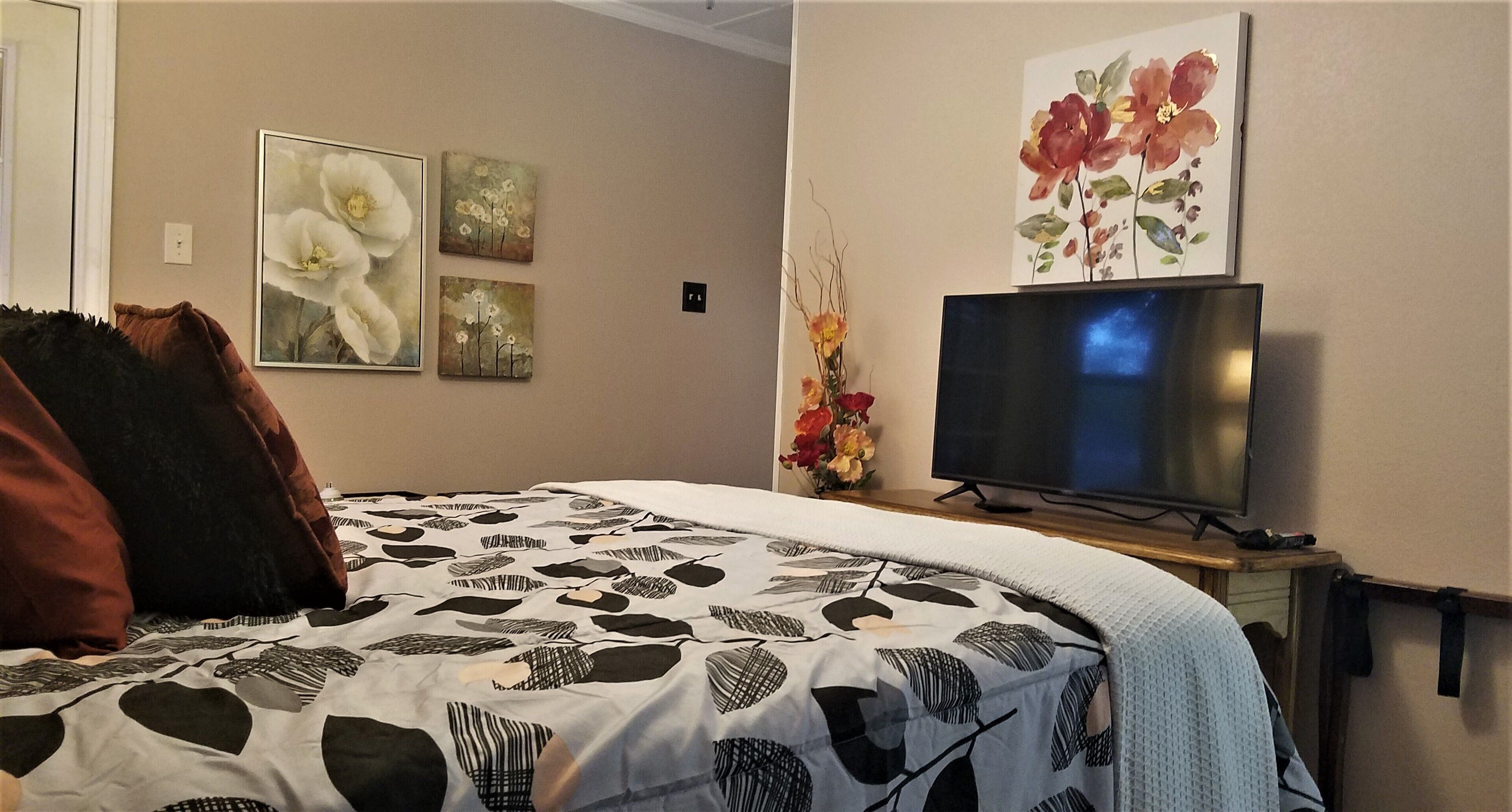 Une chambre à coucher avec un lit, une télévision et des œuvres d’art accrochées au mur.