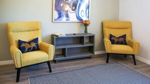Two yellow armchairs with leopard print pillows, a gray console table, and a blue abstract painting on the wall. - The Lofts at Paso Market Walk - The Elderberry Room (Paso Robles)