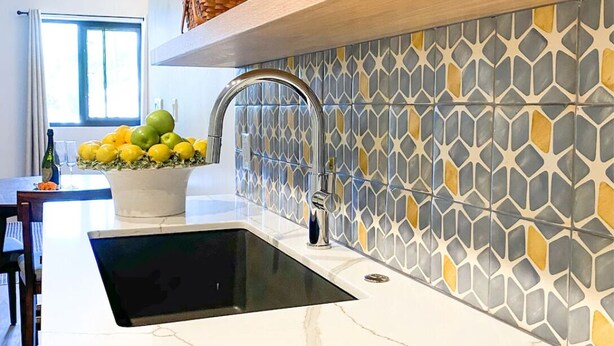A kitchen with a modern design, featuring a black sink, a stainless steel faucet, and a decorative tile backsplash with a geometric pattern. - The Lofts at Paso Market Walk - The Elderberry Room (Paso Robles)