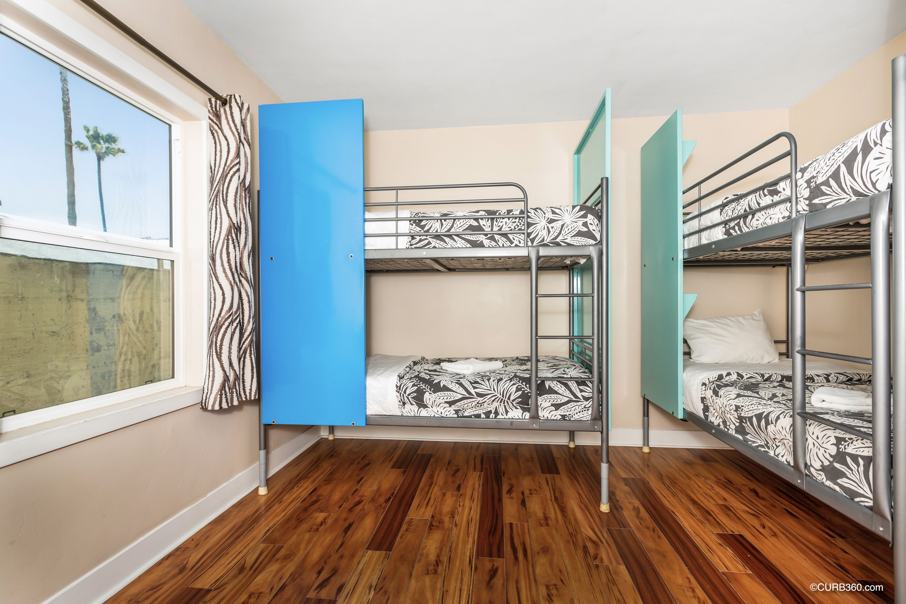A room with three bunk beds, a window with curtains, and wooden flooring.