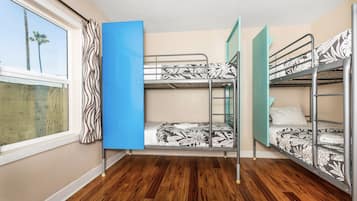A room with three bunk beds, a window with curtains, and wooden flooring.
