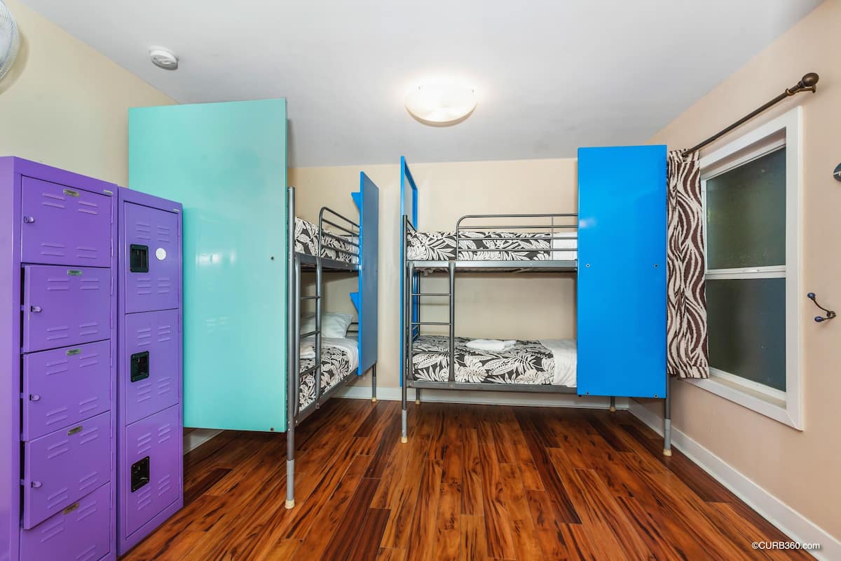 Een kamer met stapelbedden, een rij paarse kasten en een raam met een gordijn met luipaardprint.