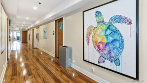 A hallway with wooden flooring, a framed artwork of a turtle, and a trash bin. - Samesun Ocean Beach - Hostel (San Diego)