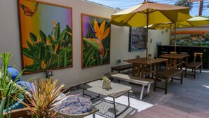 An outdoor patio with tables and chairs, surrounded by tropical plants and artwork. - Samesun Ocean Beach - Hostel (San Diego)