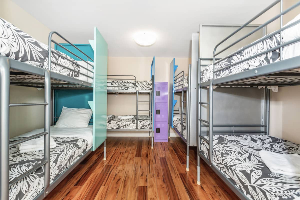 Een slaapzaal met stapelbedden, houten vloeren en een paars opbergkastje.
