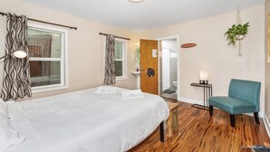 A hotel room with a bed, a chair, a small table, a plant, and a door leading to a bathroom. - Samesun Ocean Beach - Hostel (San Diego)