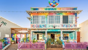 A two-story building with a colorful facade, a large peace sign above the entrance, and a pink picket fence in front. - Samesun Ocean Beach - Hostel (San Diego)