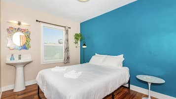 A bedroom with a bed, a round mirror, a white sink, a window with a zebra curtain, a potted plant, and a small round table.