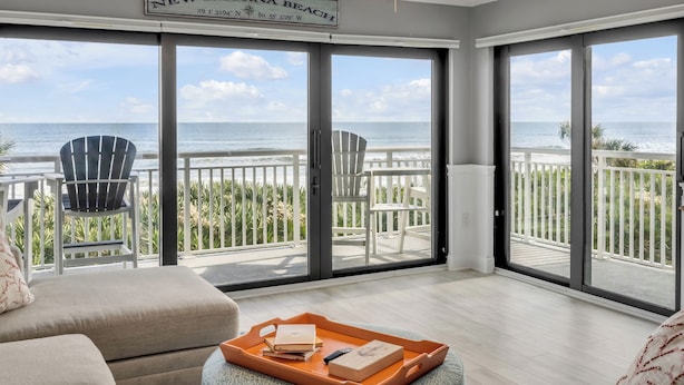 Un amplio balcón con vistas a la playa de New Smyrna, con dos sillas Adirondack y una terraza de madera.