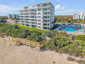 A multi-story hotel with balconies, a swimming pool, and a beach area.