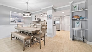 Una cocina moderna con armarios blancos, una isla central y un comedor con mesa y sillas de madera.