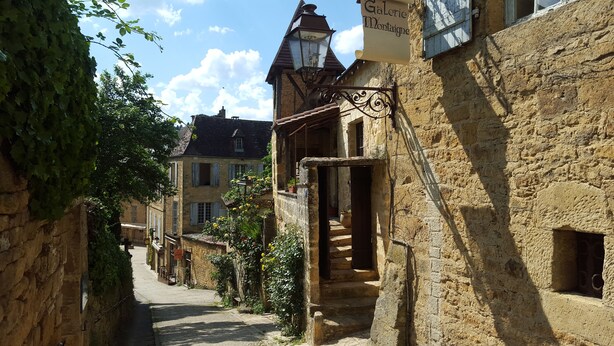 A narrow street with stone buildings, a visible entrance to a building, and a sign that reads "Galerie Montagne".