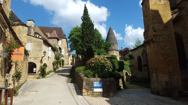 A narrow cobblestone street flanked by historic stone buildings with a church tower in the distance.