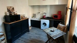 A compact kitchen with a washing machine, a microwave, and a red coffee maker. There's a stop sign on the wall and a wicker chair in the corner. - Private mansion (Béziers)