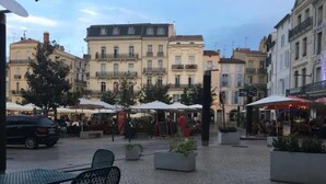 An outdoor café area with tables and chairs, surrounded by buildings with balconies and windows. - Private mansion (Béziers)