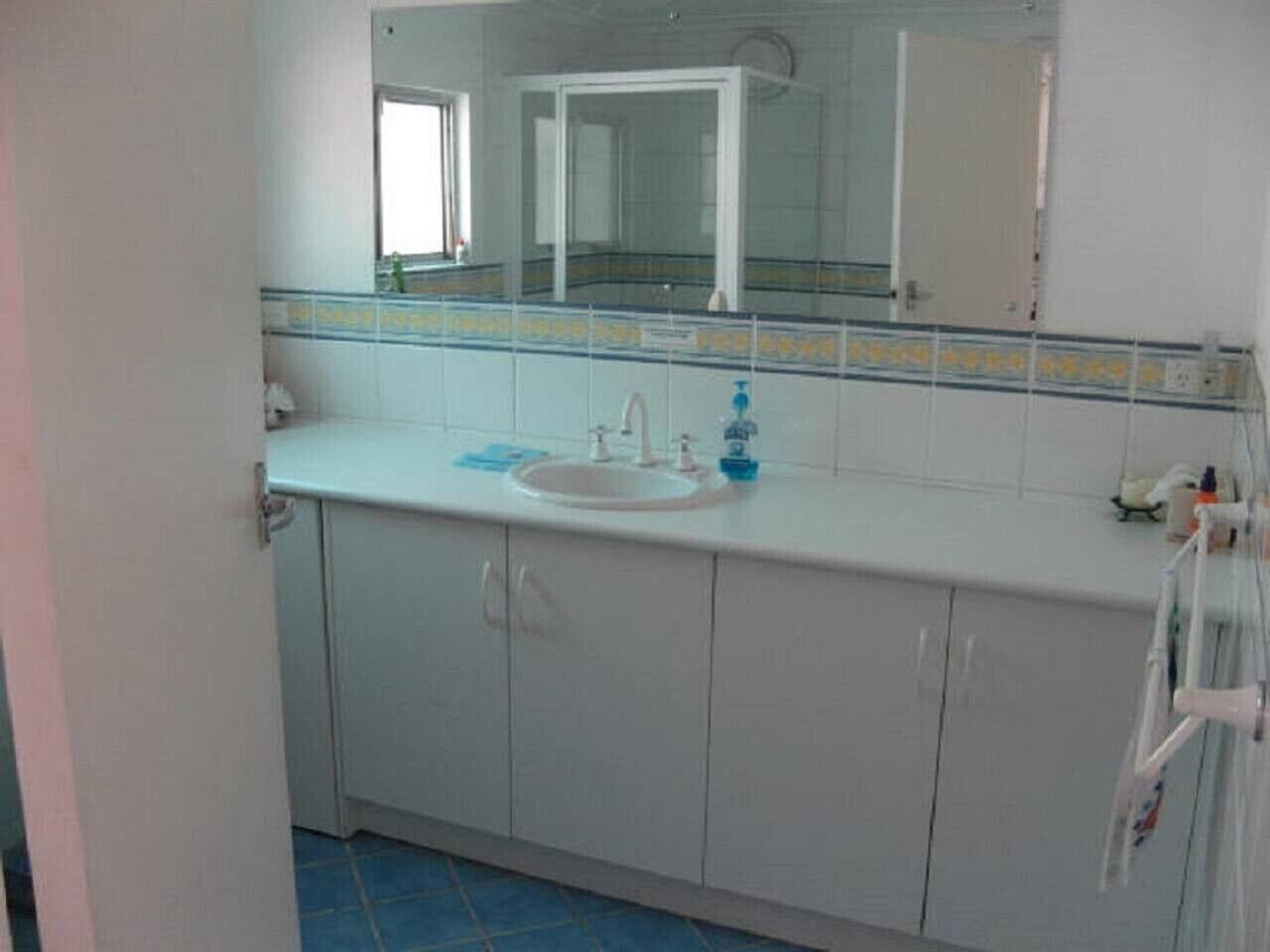 Un baño con un lavamanos, espejo y armarios blancos.