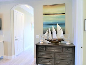 A hallway with a dark wooden dresser, a sailboat model, and a painting of a seascape.