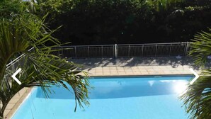 A rectangular swimming pool with a tiled deck surrounding it, enclosed by a metal fence.