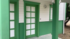 A building with green doors and white trim, a tiled entrance, and a small window with a light fixture.