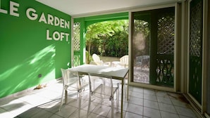 A patio area with a table and chairs, a green wall, and a sliding glass door leading to a garden.