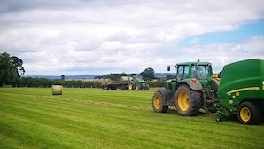 A green tractor with yellow wheels in a grassy field, with hay bales and another tractor in the background. - Burton Grange Farmhouse B&B (York)