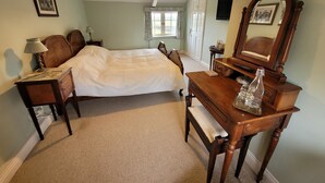 A bedroom with a bed, a wooden dresser, a nightstand, a lamp, a mirror, and a window with curtains. - Burton Grange Farmhouse B&B (York)